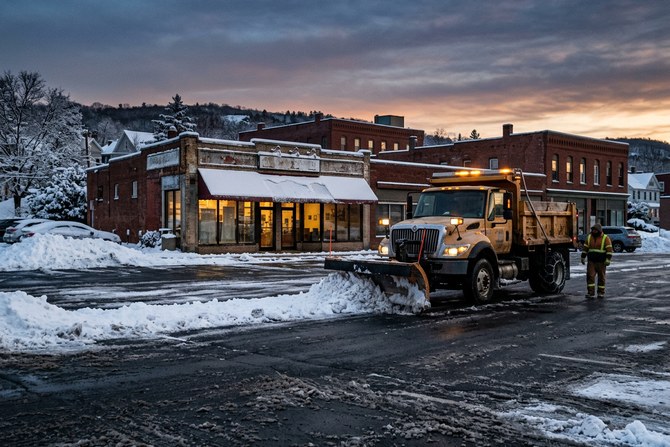 Snow plow truck clearing snow from a commercial parking lot at dawn
