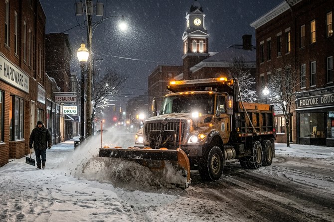 Snow removal truck with plow blade working through heavy snow at night